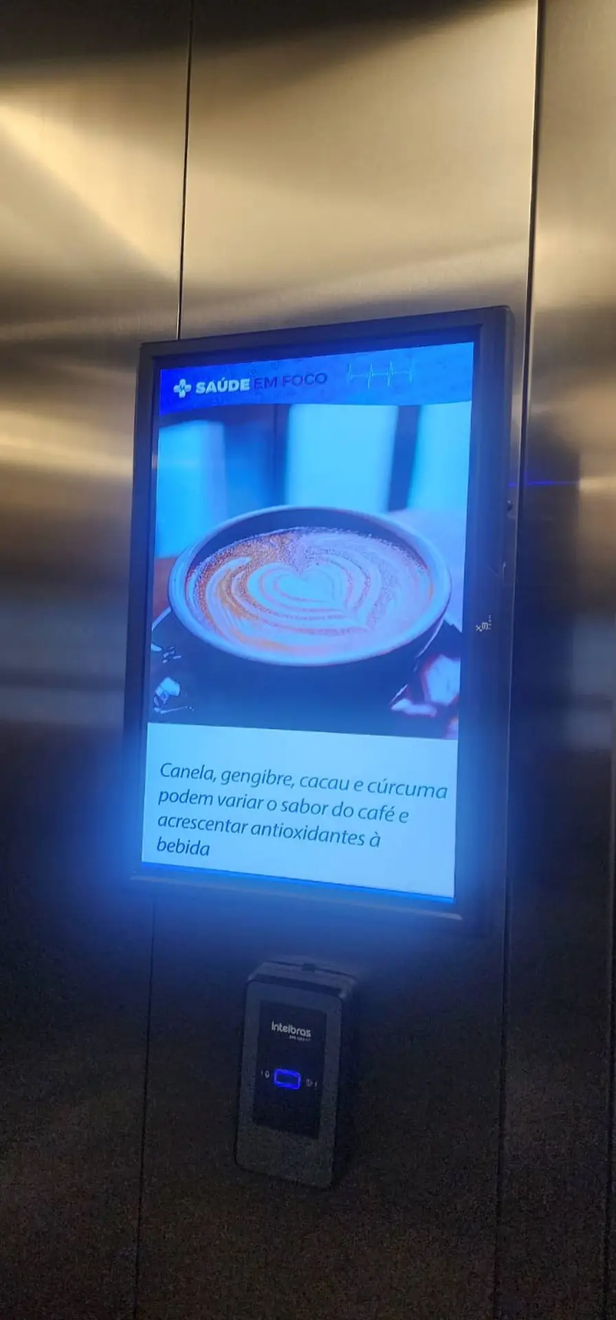 Home Tela digital em elevador do Condomínio Ibirapitã exibindo campanha Saúde em Foco com dicas de saúde e qualidade de vida.